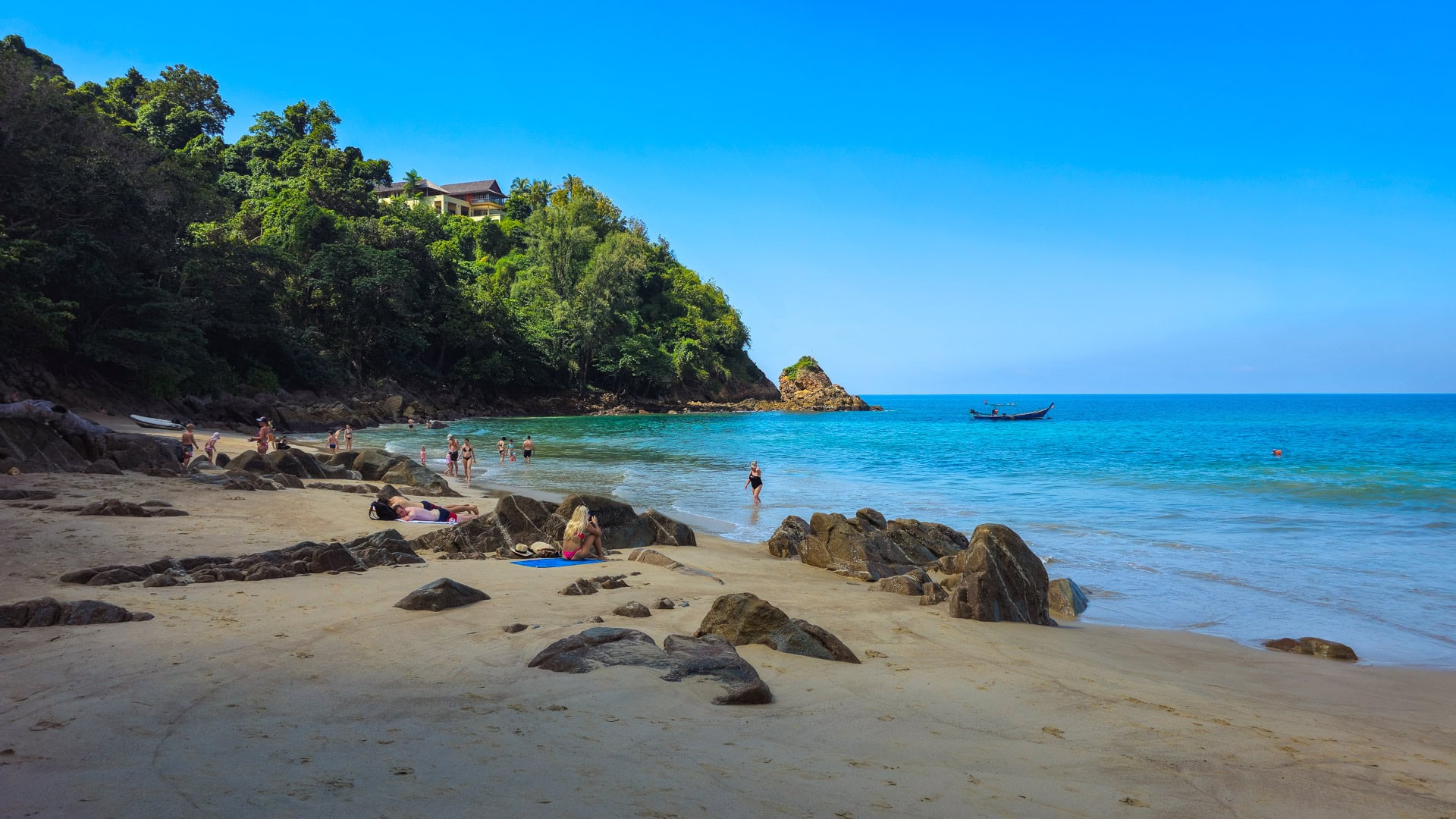 Rocky cove with swimmers and clear water below forested hillside at Banana Beach Phuket.