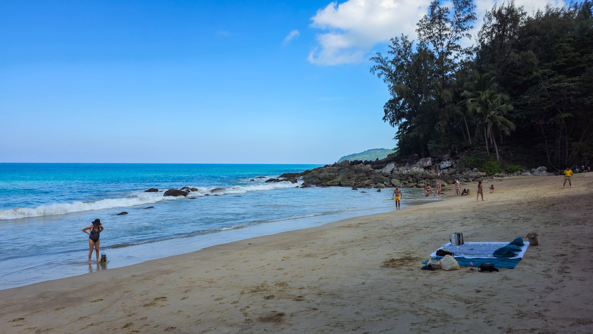 Sandy cove with longtail boat offshore and rock formations near low tide.