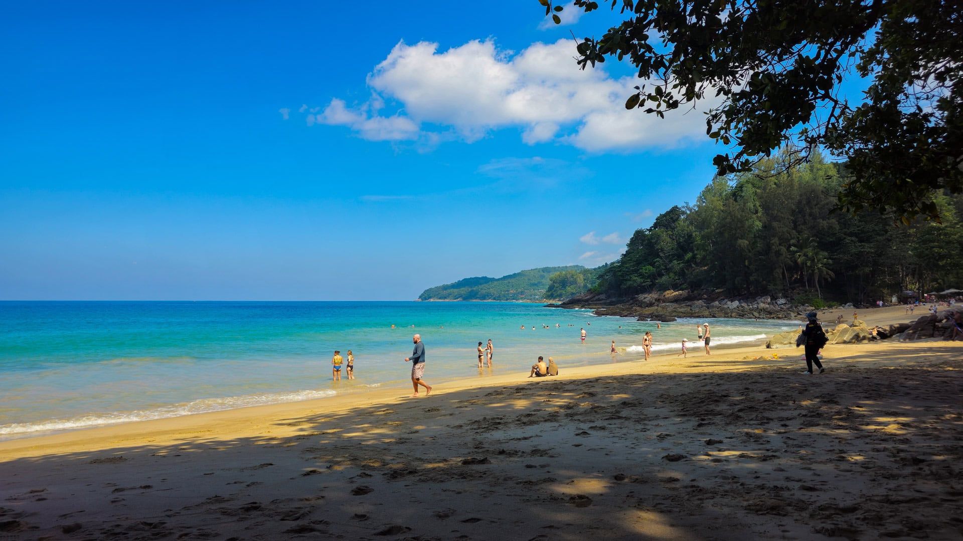 Central part of Banana Beach Phuket with swimmers near shore and rocky headland.
