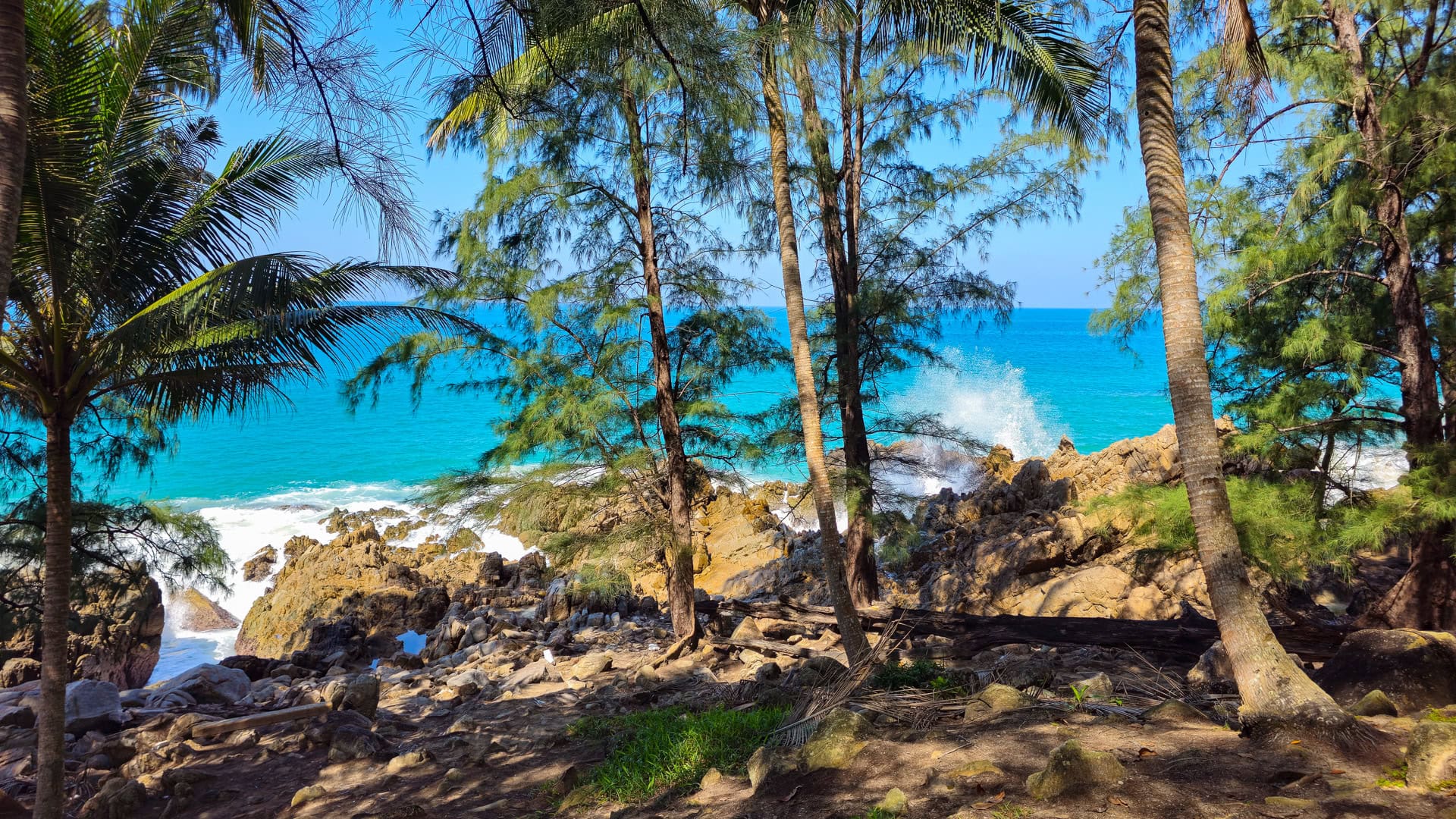 Elevated viewpoint over Banana Beach Phuket with turquoise waves and rocky shallows.