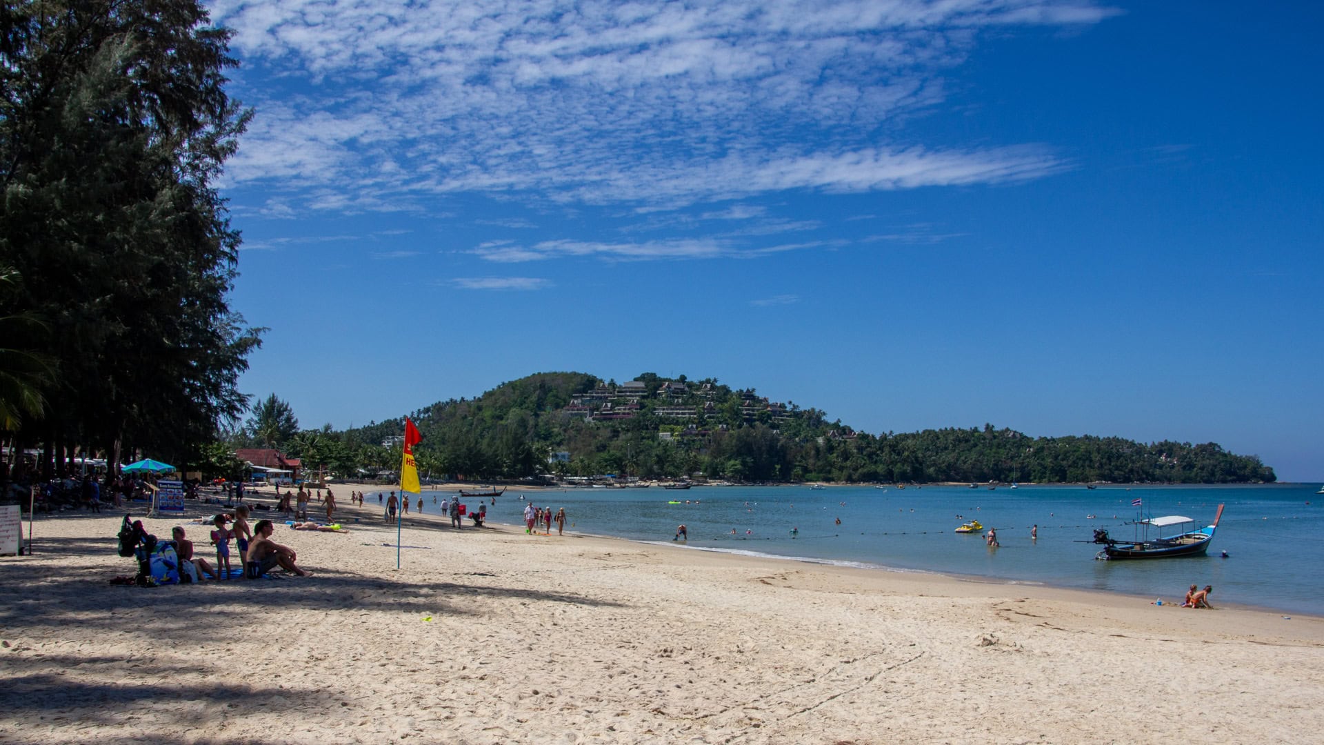 Bang Tao Beach Phuket soft sand, family swimmers, calm blue water and hillside villas behind the bay.
