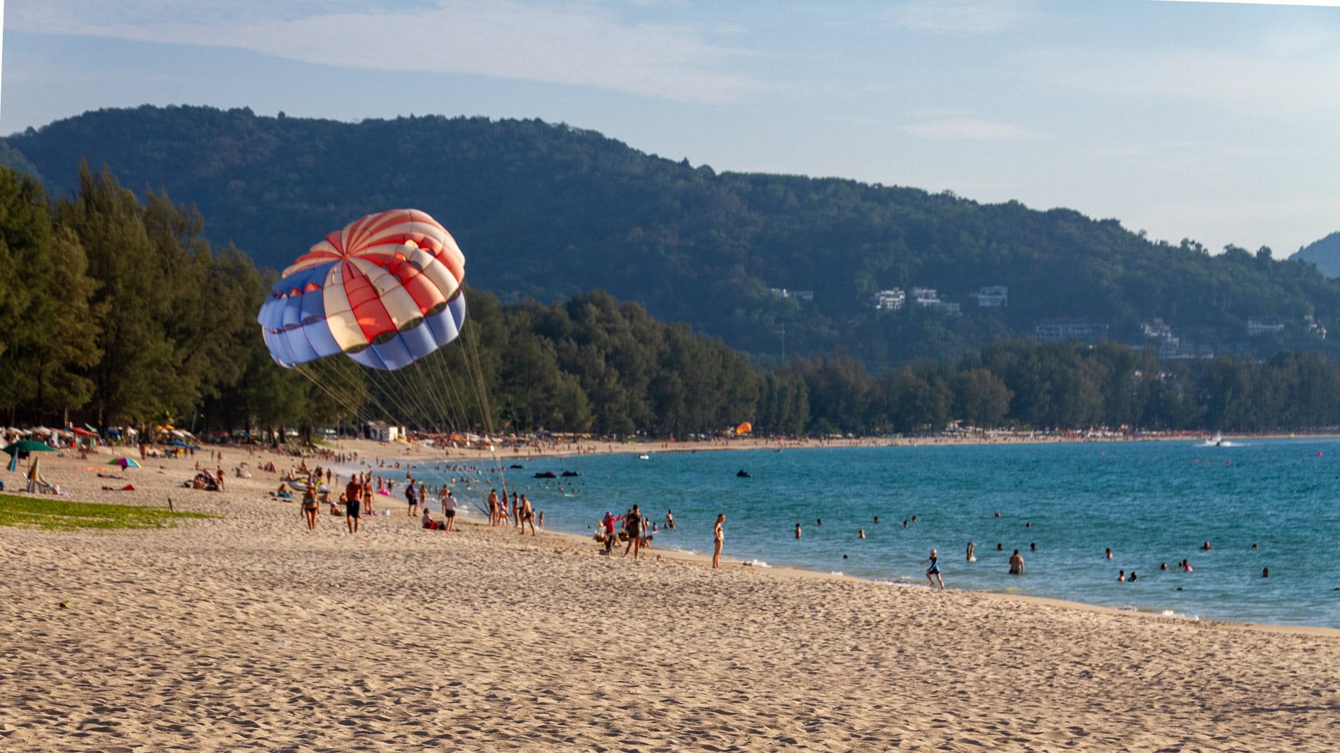 Parasail activity off Bang Tao Beach with hills and forest behind.