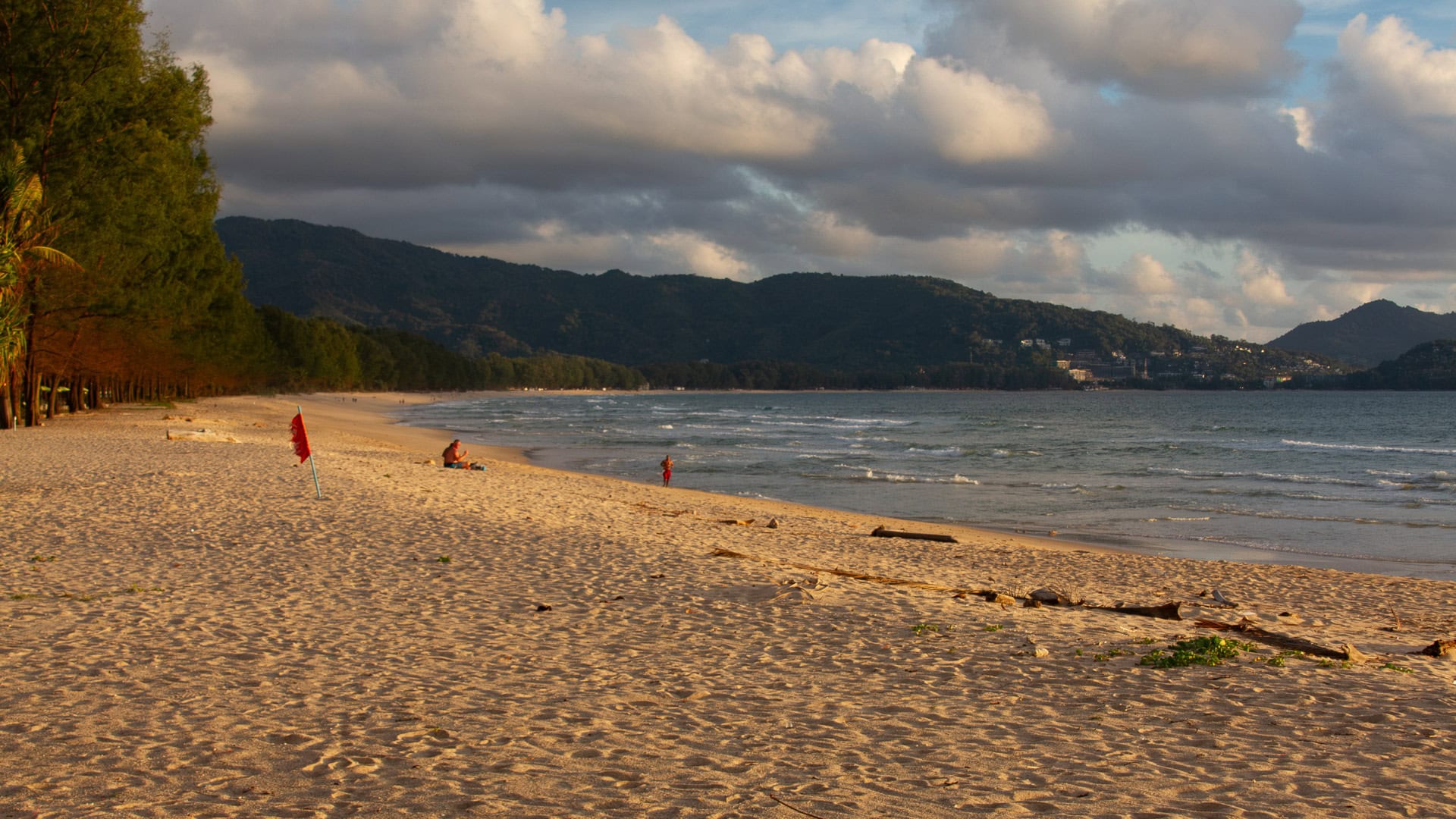 Evening light on sandy beach with small waves and hills in the distance.