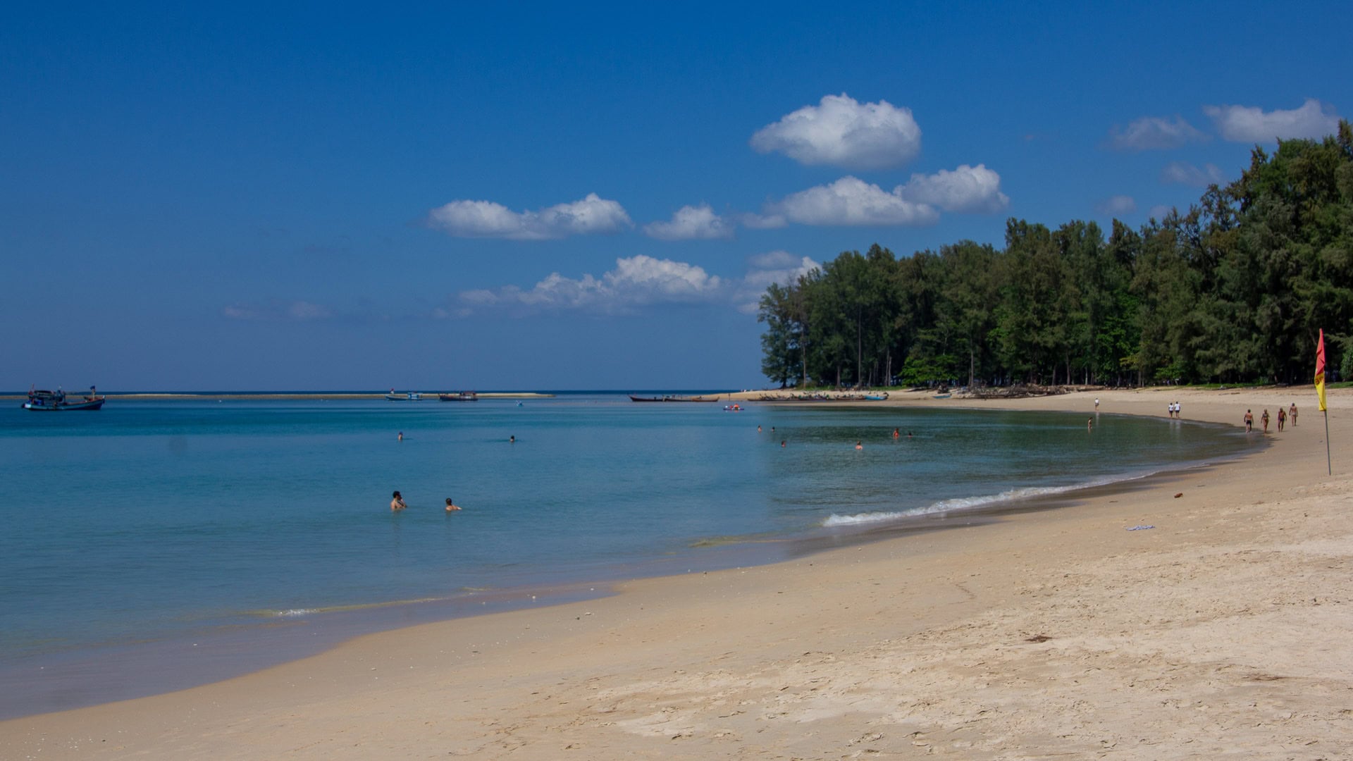 Locals walking along the shallow shoreline of Nai Yang Beach Phuket, framed by sea pines.