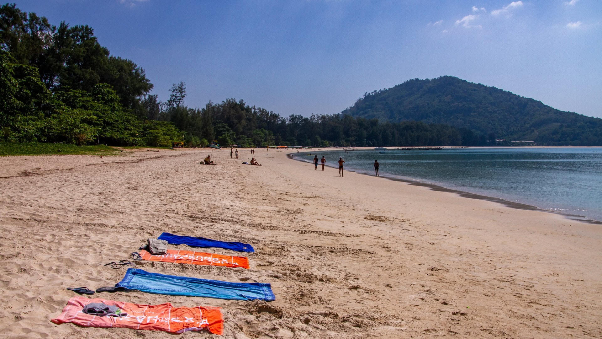 Beach umbrellas and visitors enjoying the shaded area of Nai Yang Beach Phuket under tall casuarina trees.
