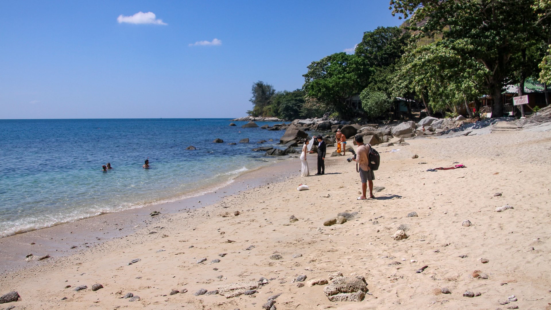 Ao Sane Beach Phuket sandy shoreline with scattered rocks and people walking near the water