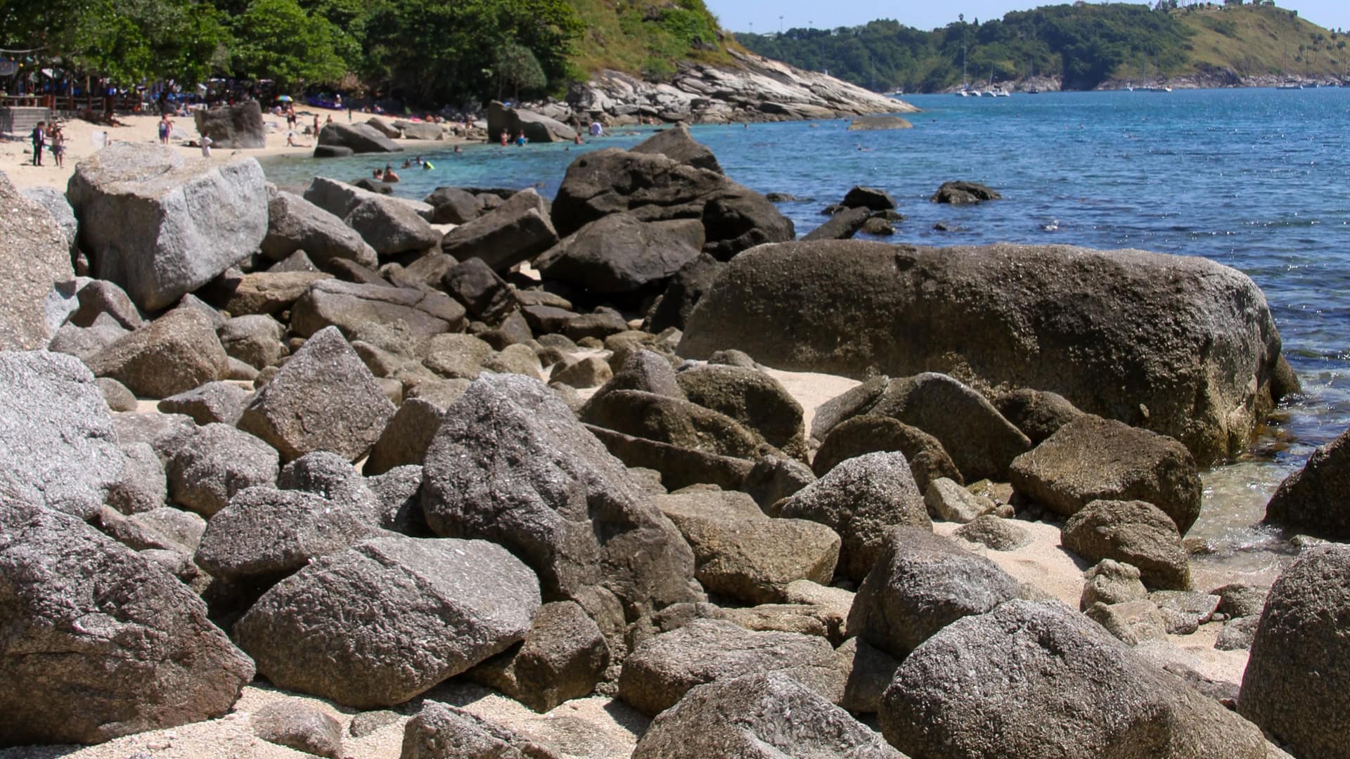 Ao Sane Beach Phuket shoreline with large boulders and people swimming