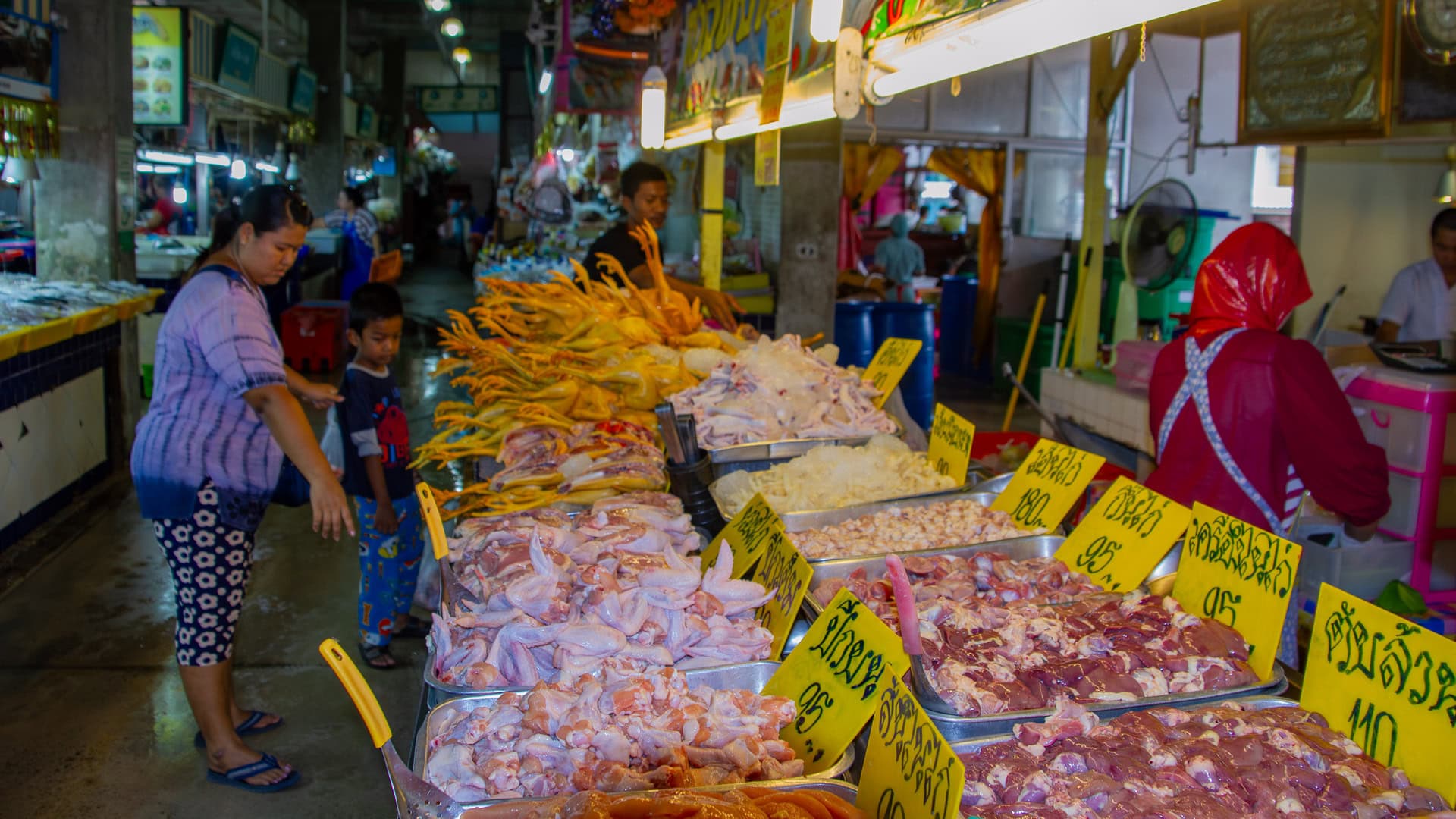Banzaan Fresh Market Phuket meat section with raw poultry and pork displayed while a vendor cuts portions.