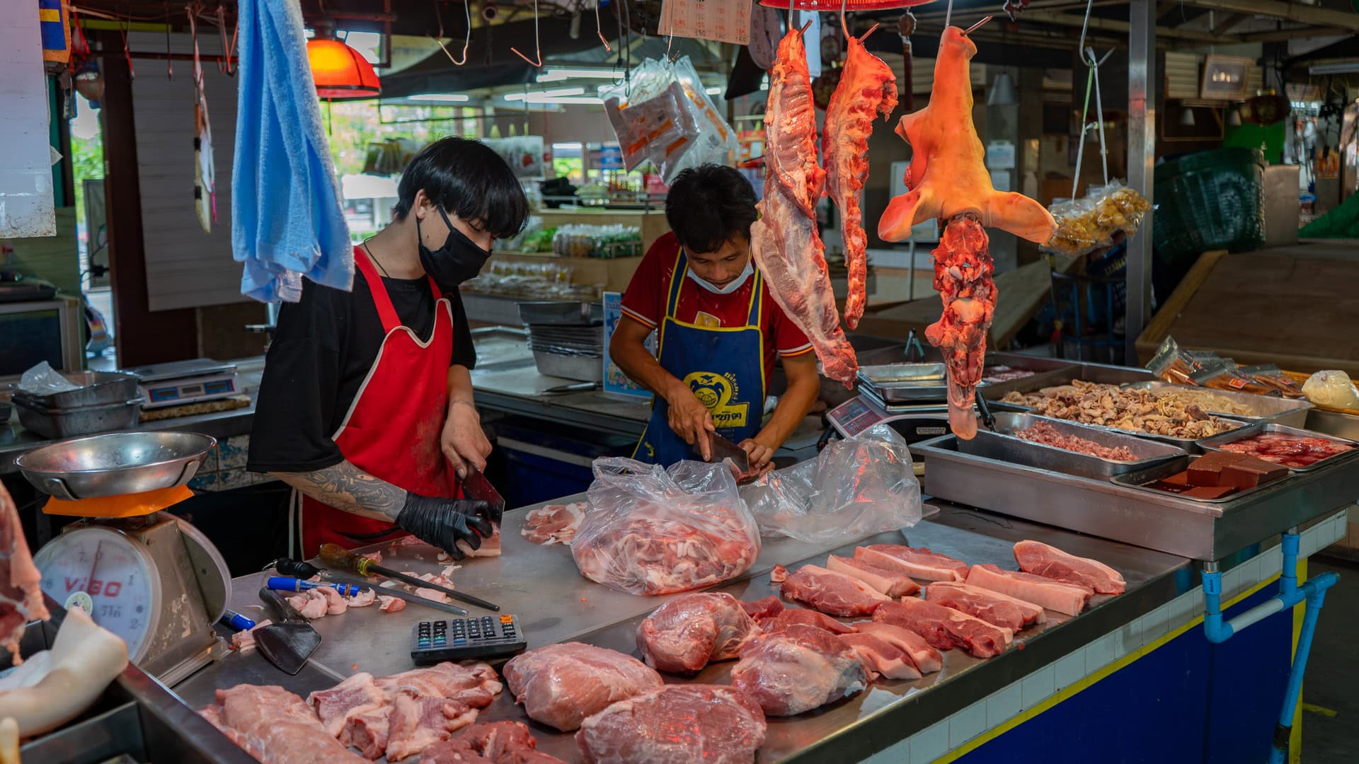 Banzaan Fresh Market Phuket butcher counter with vendors trimming and weighing pork on a stainless steel table.