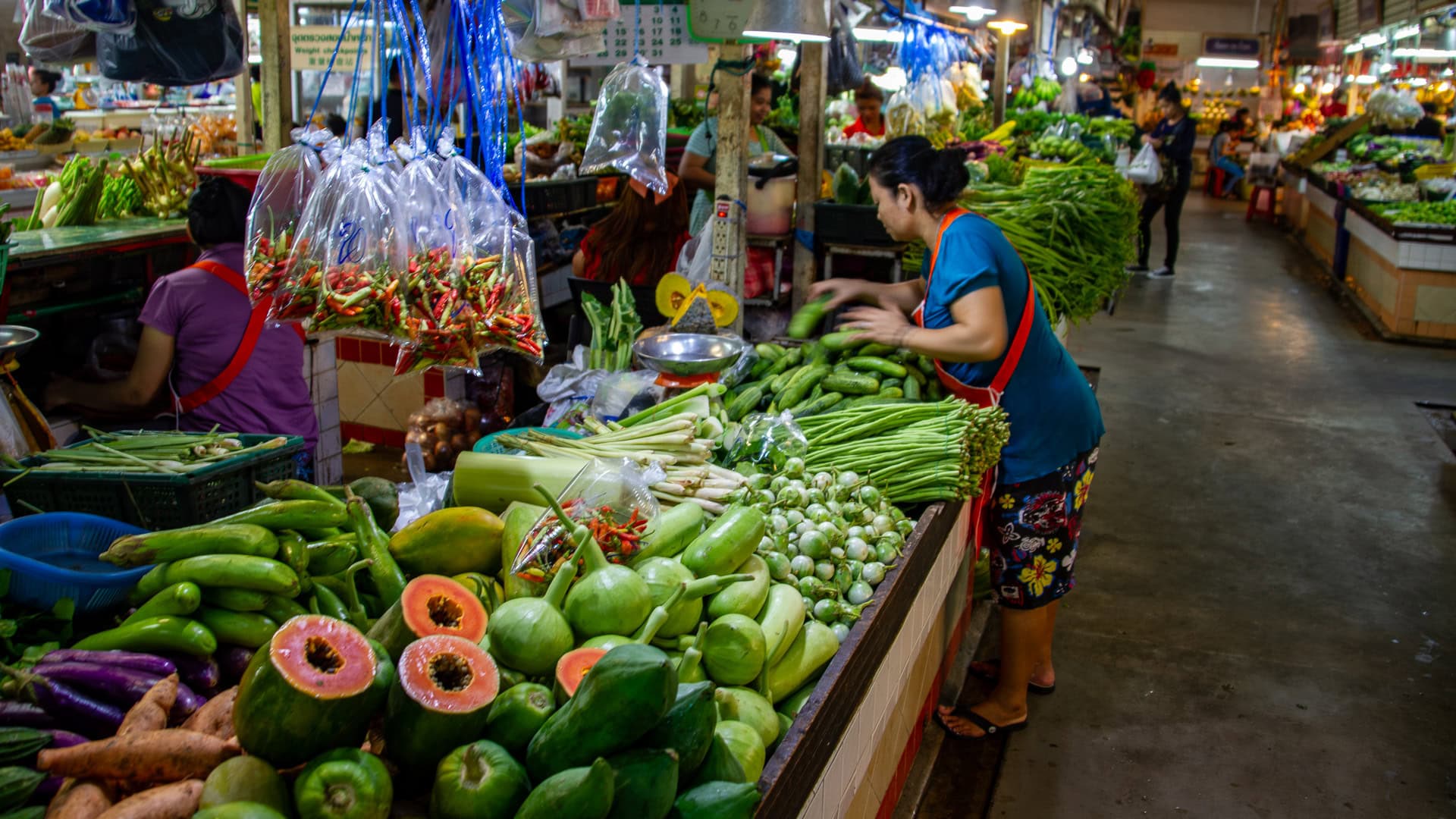 Banzaan Fresh Market Phuket vegetable stalls with green produce arranged on counters and hanging bags of chilies.