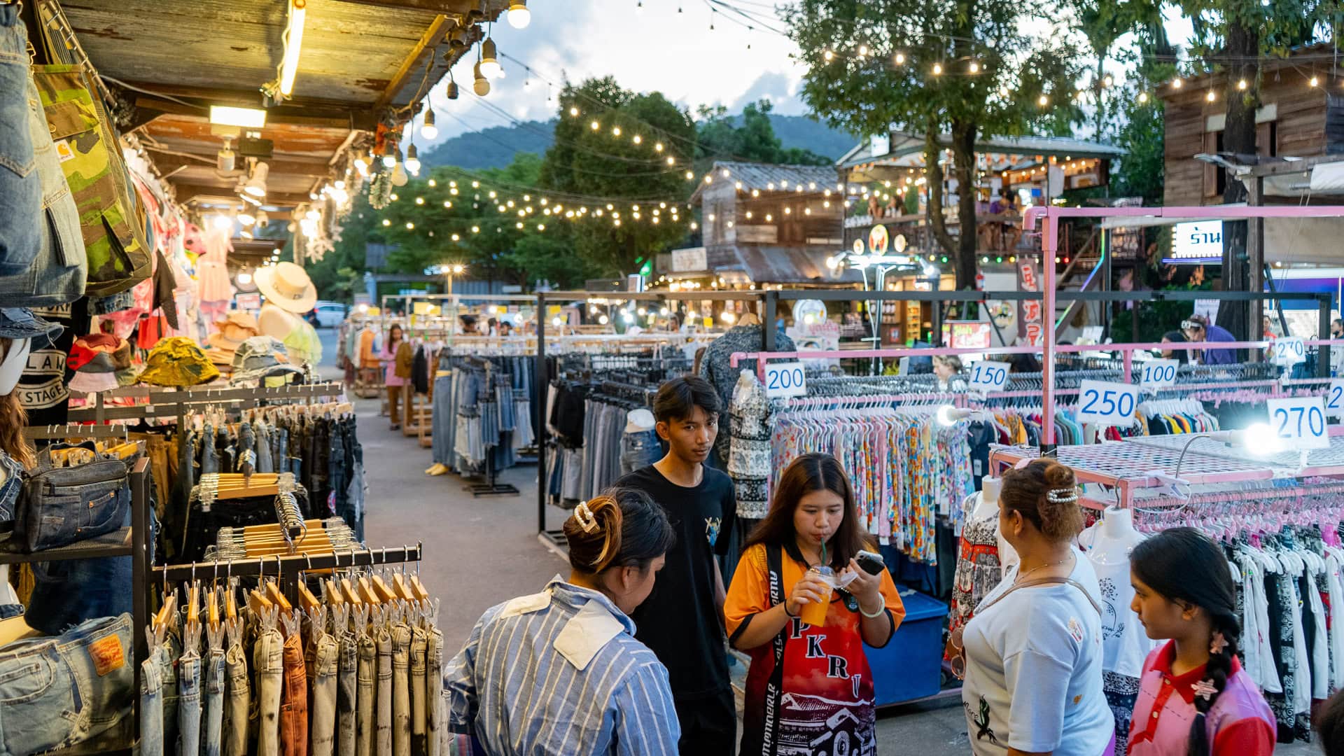Chillva Market Phuket with clothing stalls, rows of hanging garments, price signs above racks, and people standing and browsing along the walkway.