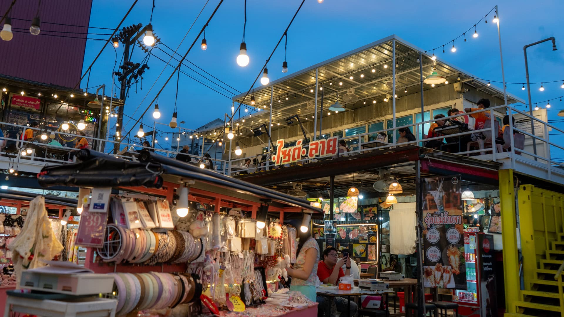 Chillva Market Phuket with food and retail stalls at ground level, an upper-level seating area with people eating, and overhead lights spanning the market space.