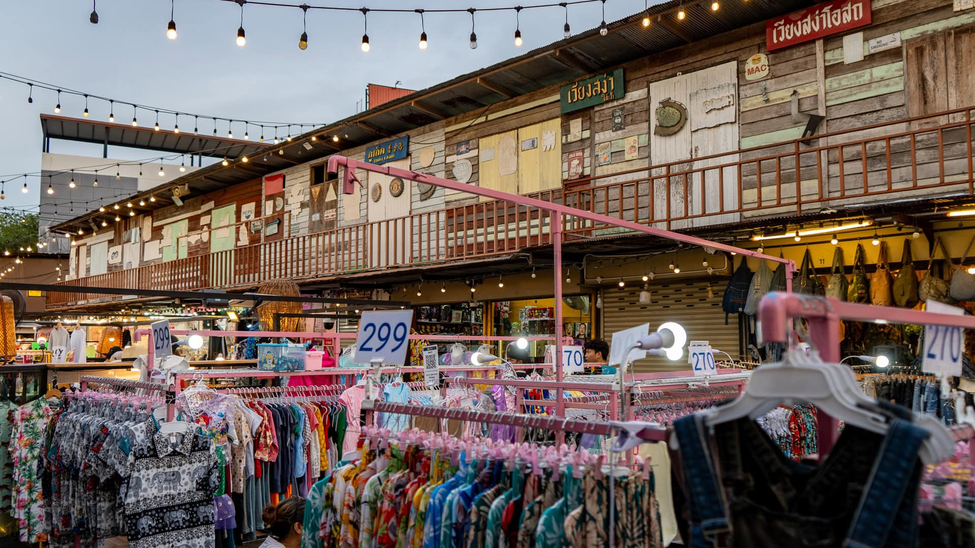 Chillva Market Phuket with a two-storey wooden market building, balcony walkway, hanging signs, and clothing stalls arranged below.