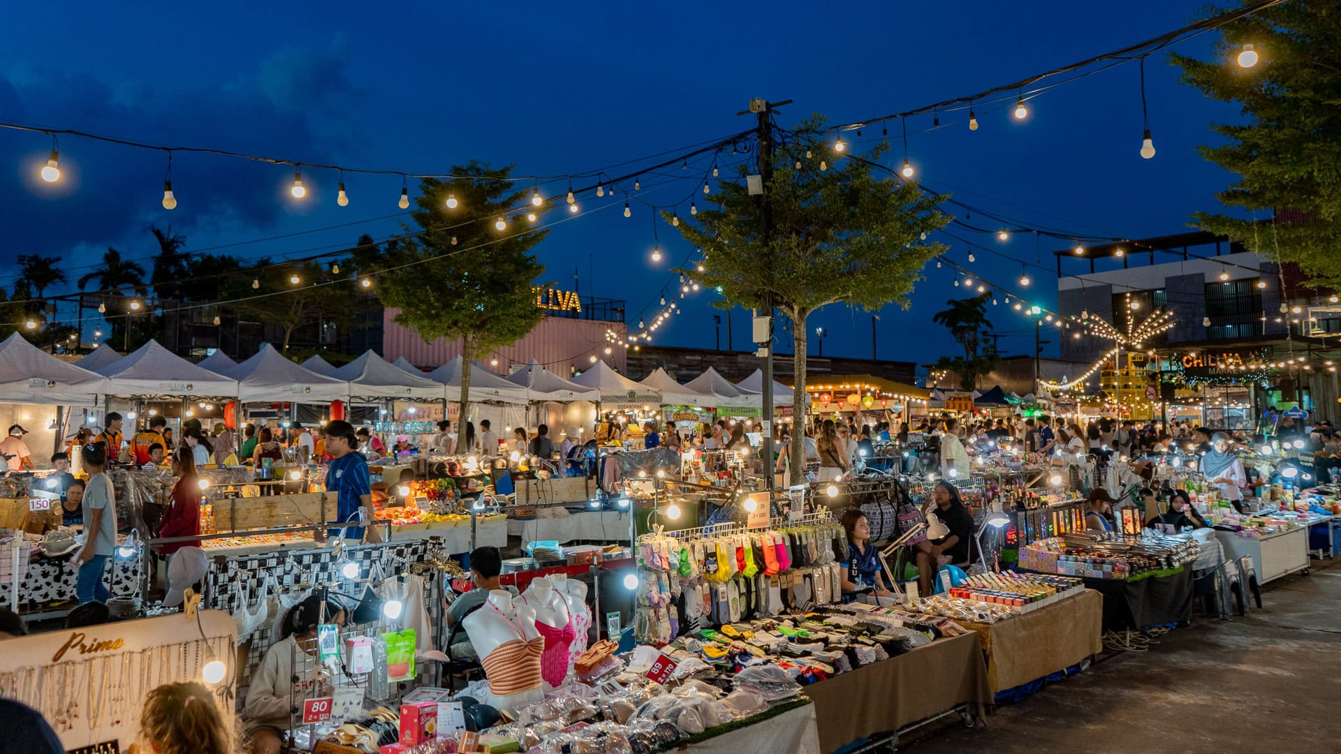 Chillva Market Phuket with stalls selling small accessories, phone cases, hair items, and assorted goods, with people browsing under overhead lights.