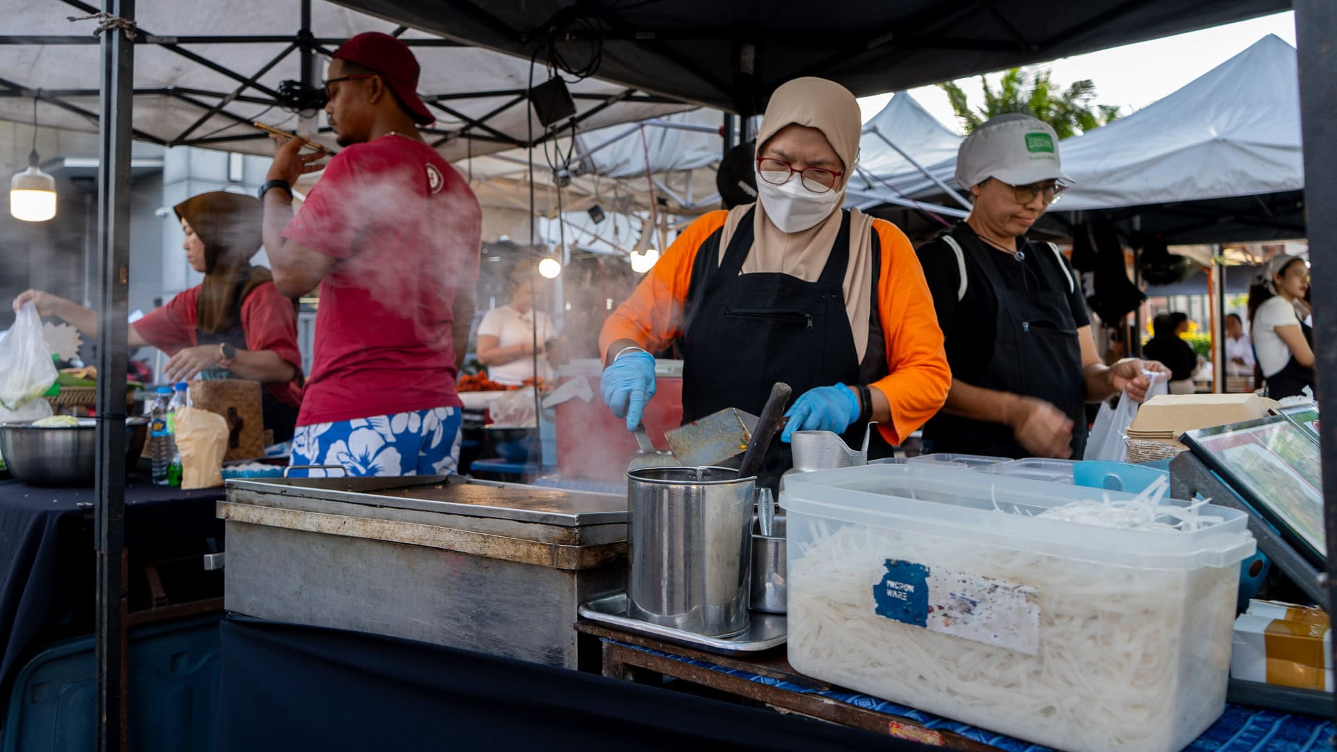 Fun Friday Boat Avenue Market Phuket hot food stall with vendors cooking noodles on a flat grill, steam rising from the cooking surface and containers of ingredients placed on the counter