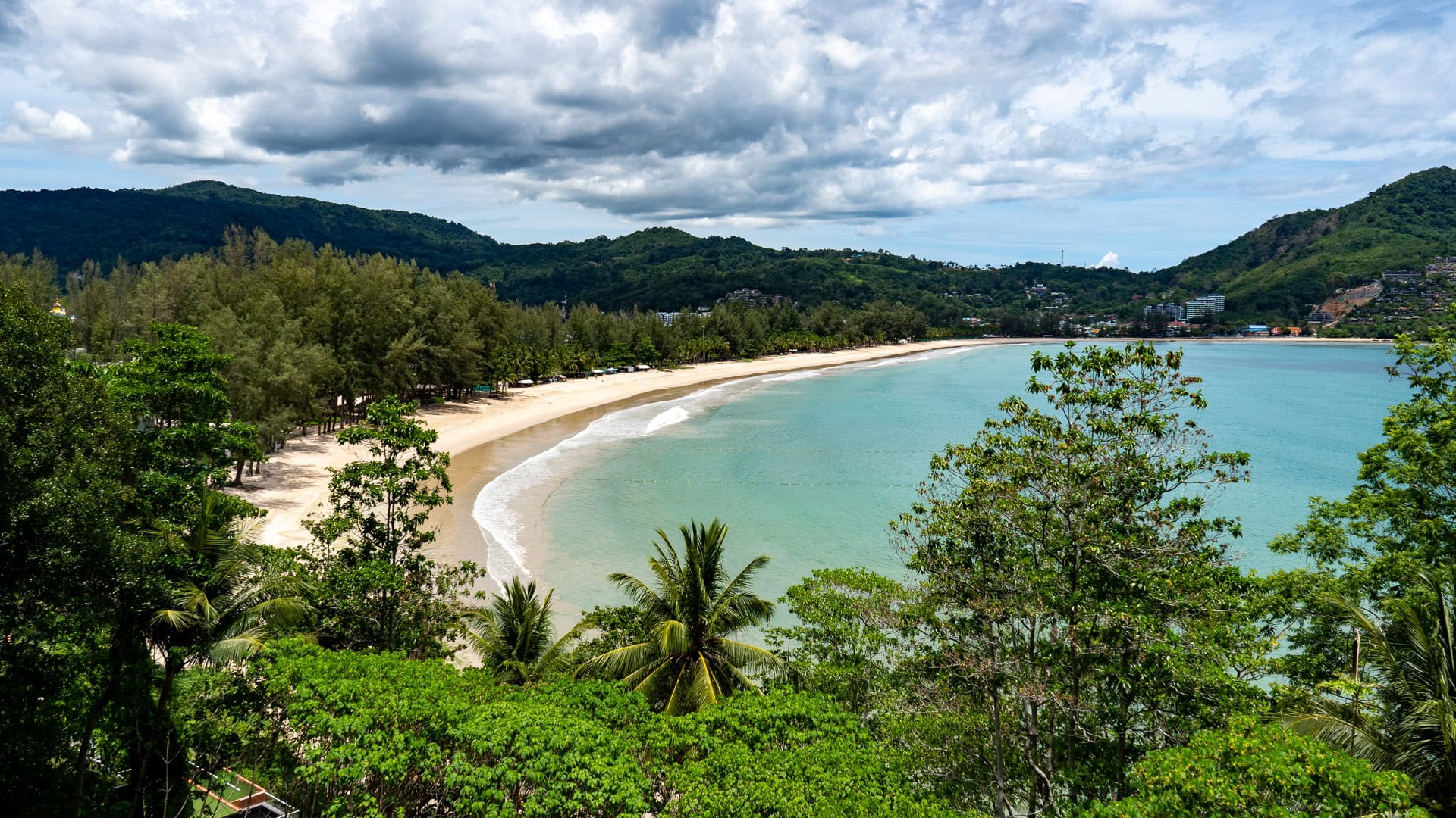 Central shoreline of Kamala Beach Phuket with soft sand and calm dry-season water.