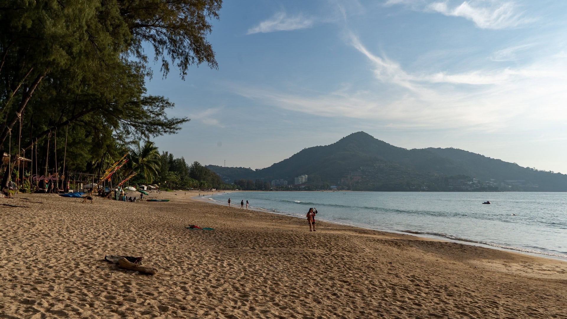 Wide-angle view of Kamala Beach Phuket showing palm-lined edges and gentle waves.