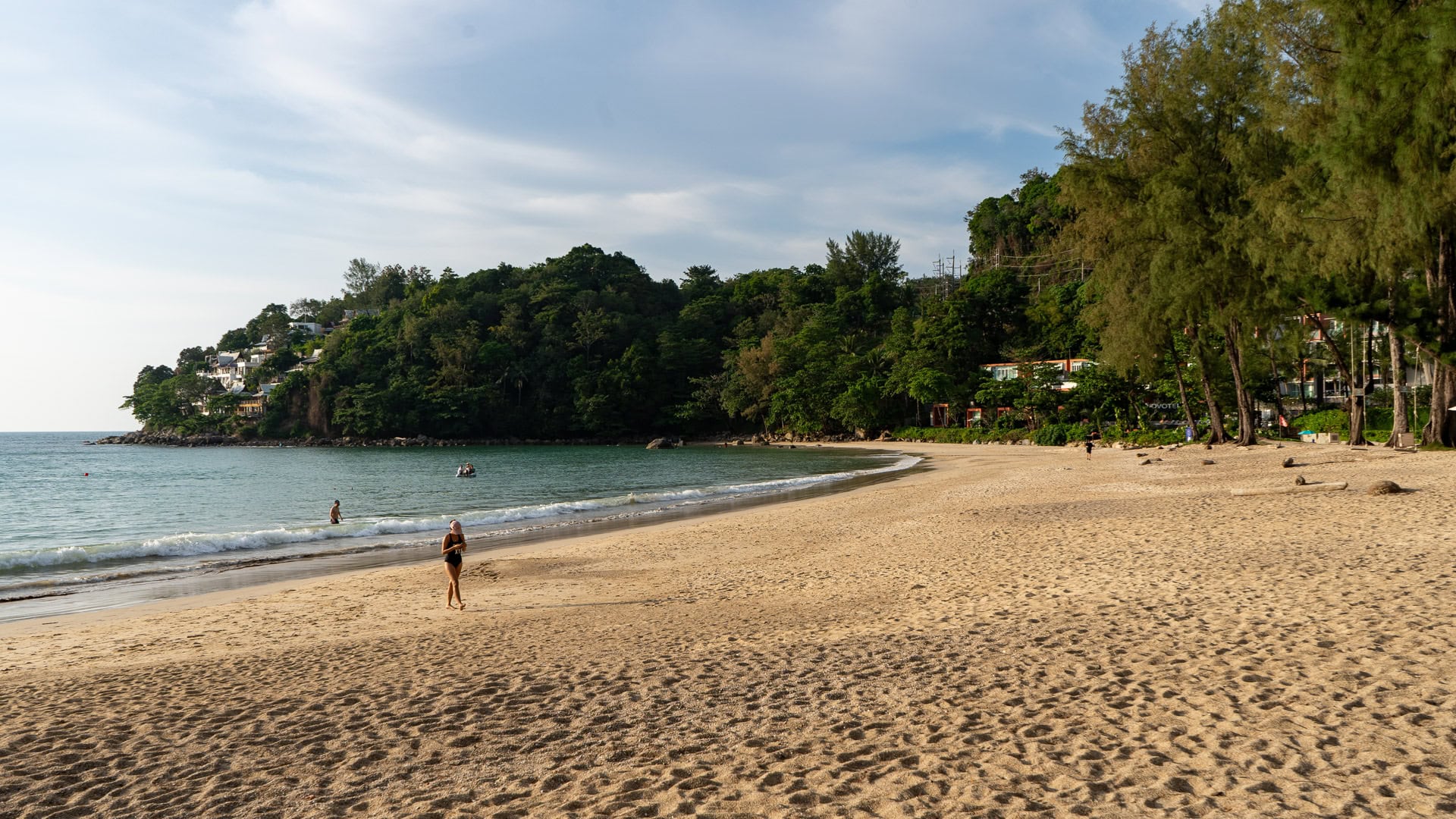 Northern end of Kamala Beach Phuket with sand, headland backdrop and clear water.