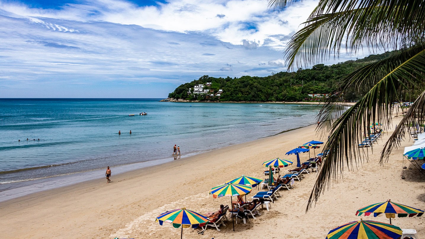 Long stretch of Kamala Beach Phuket with people walking along the waterline.