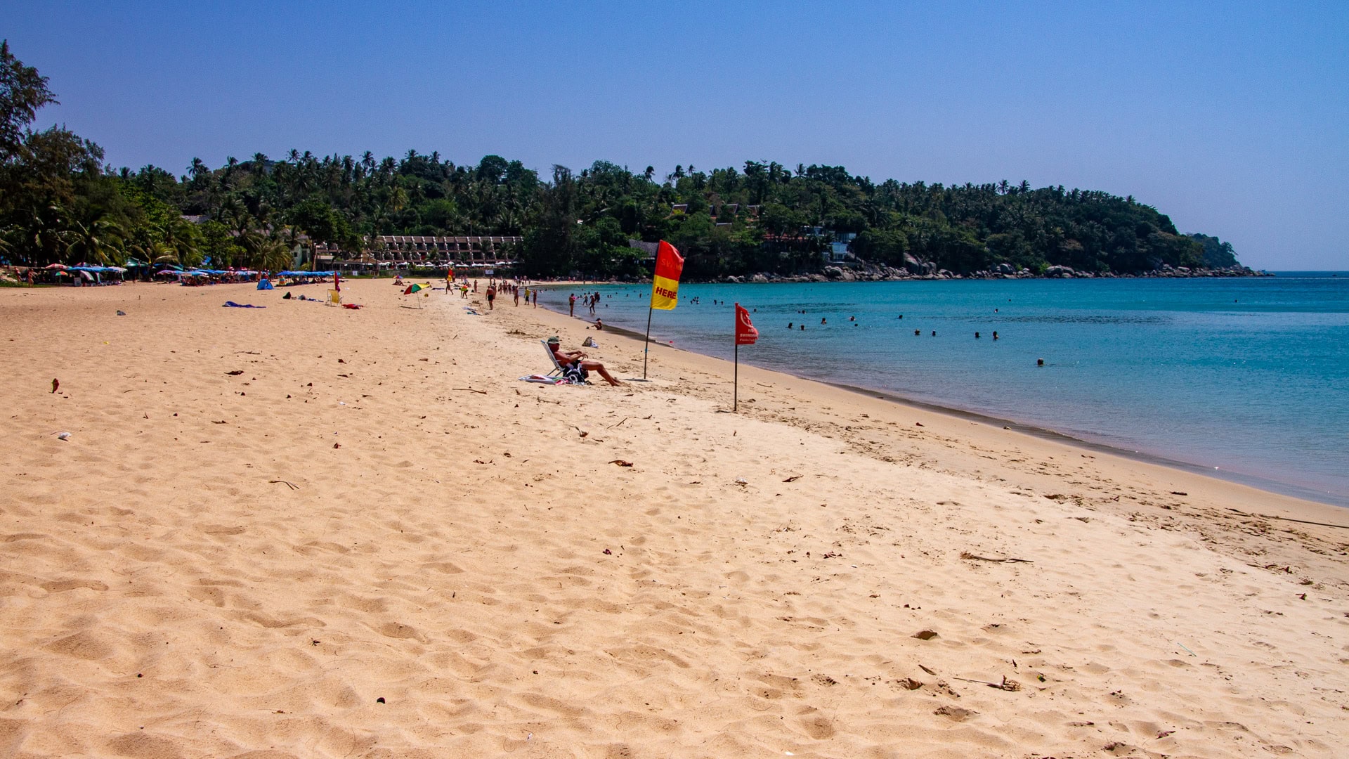 Sandy shoreline at Karon Beach Phuket with red and yellow warning flags