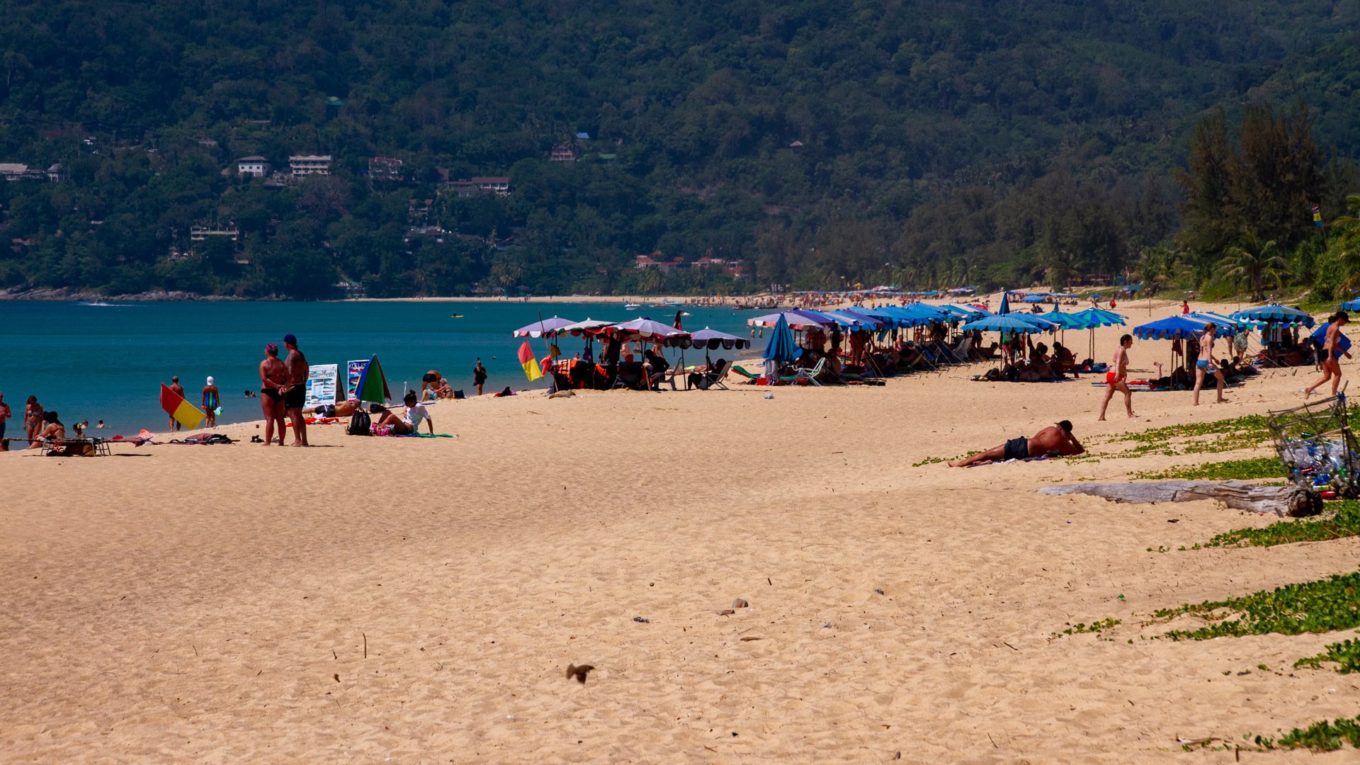 Busy section of Karon Beach Phuket with umbrellas, sunbeds, and beachgoers