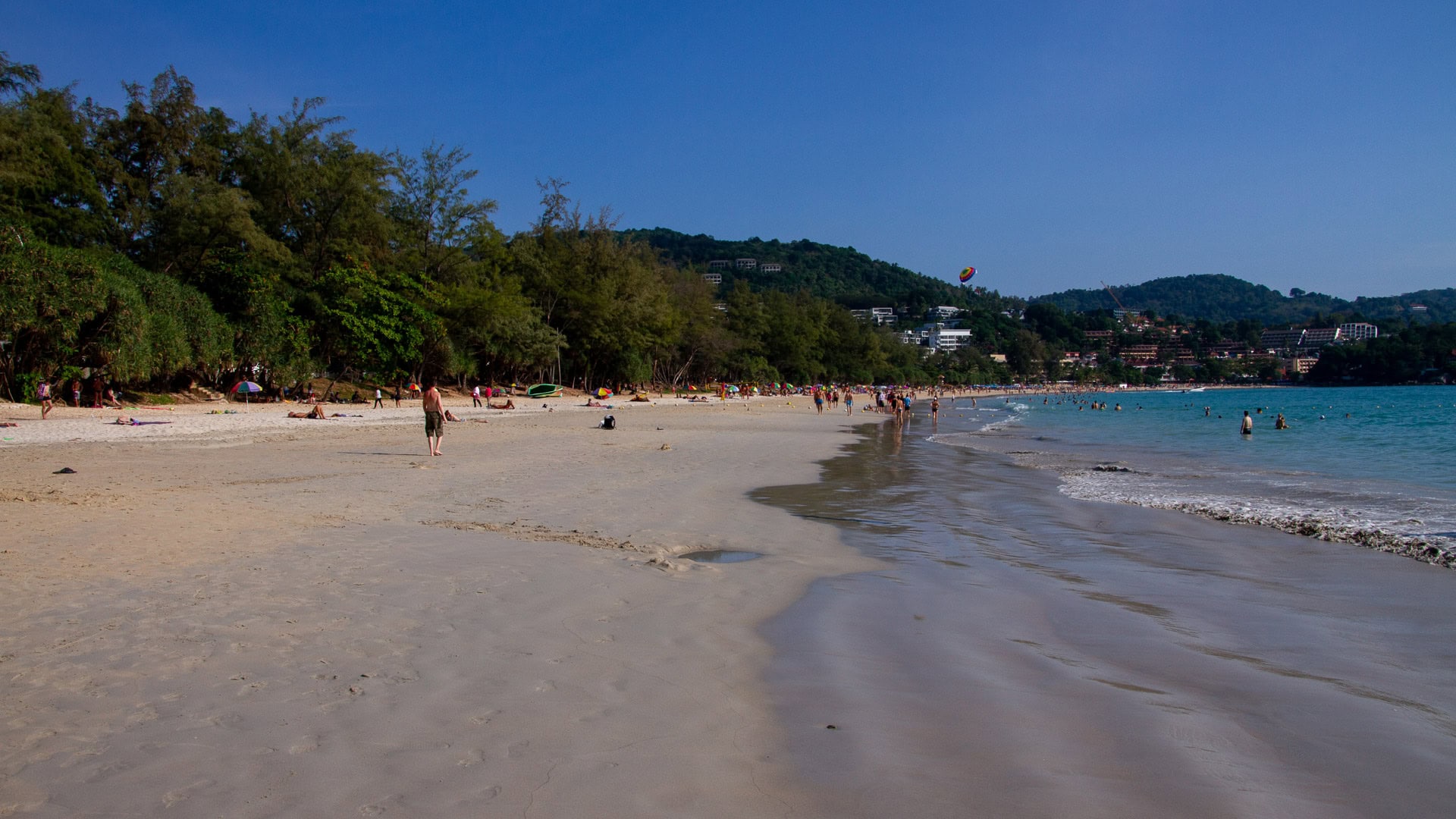 Kata Beach Phuket wide shoreline with wet sand, calm water, and people walking along the waterline