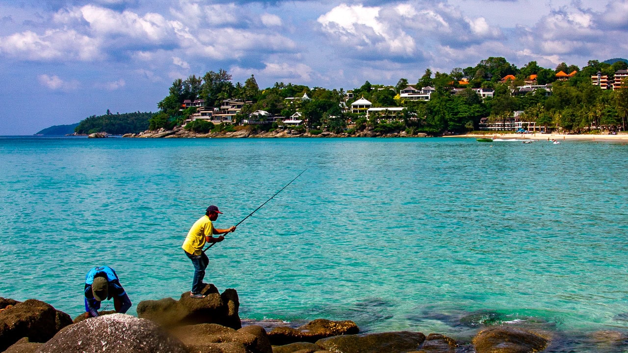 Kata Noi Beach Phuket rocky shoreline with clear turquoise water and fishing activity