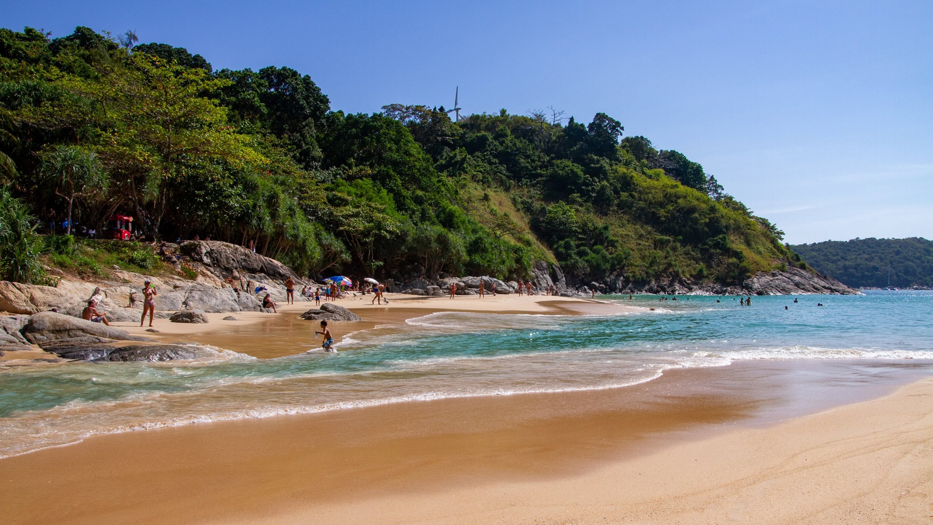 Nai Harn Beach Phuket shoreline with gentle waves, swimmers, and forested headland