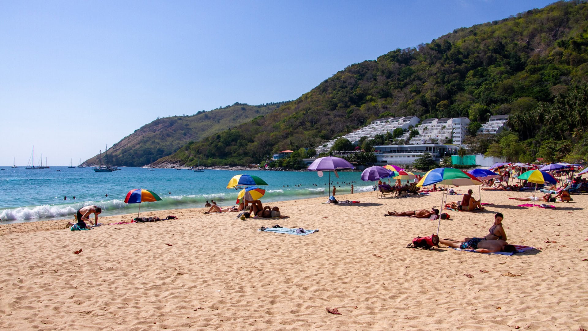 Nai Harn Beach Phuket wide sand area with sunbathers and hillside buildings in background