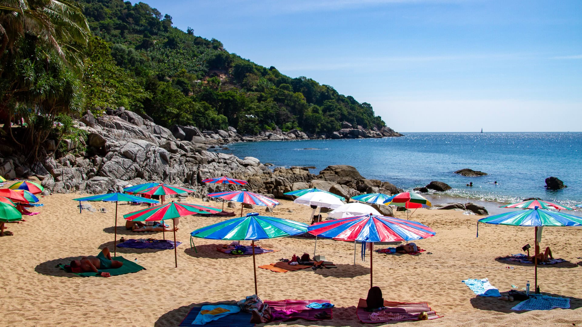 Nui Beach Phuket colorful beach umbrellas on sand with rocky headland behind