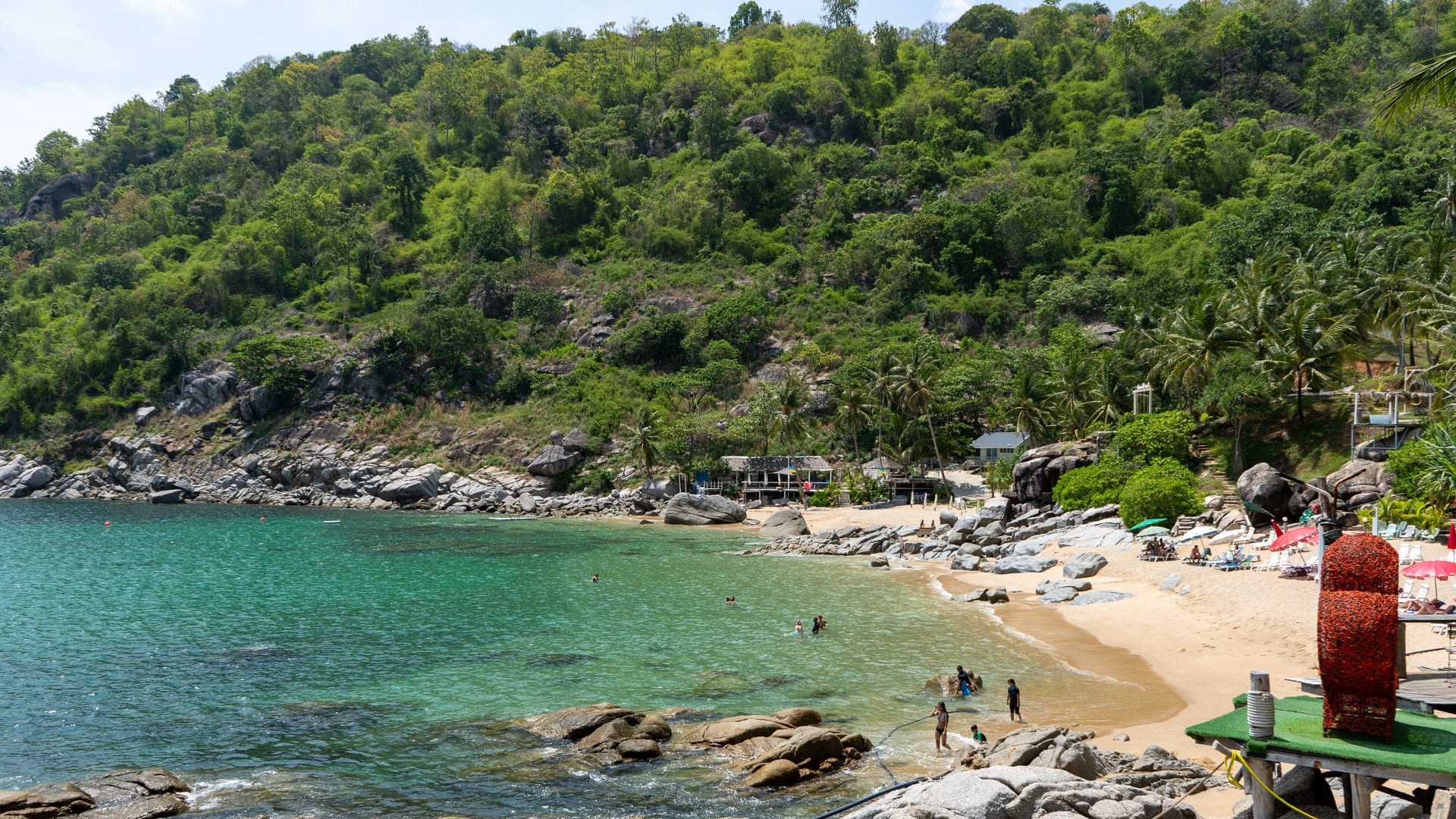 Nui Beach Phuket sun loungers with red umbrellas along narrow beach