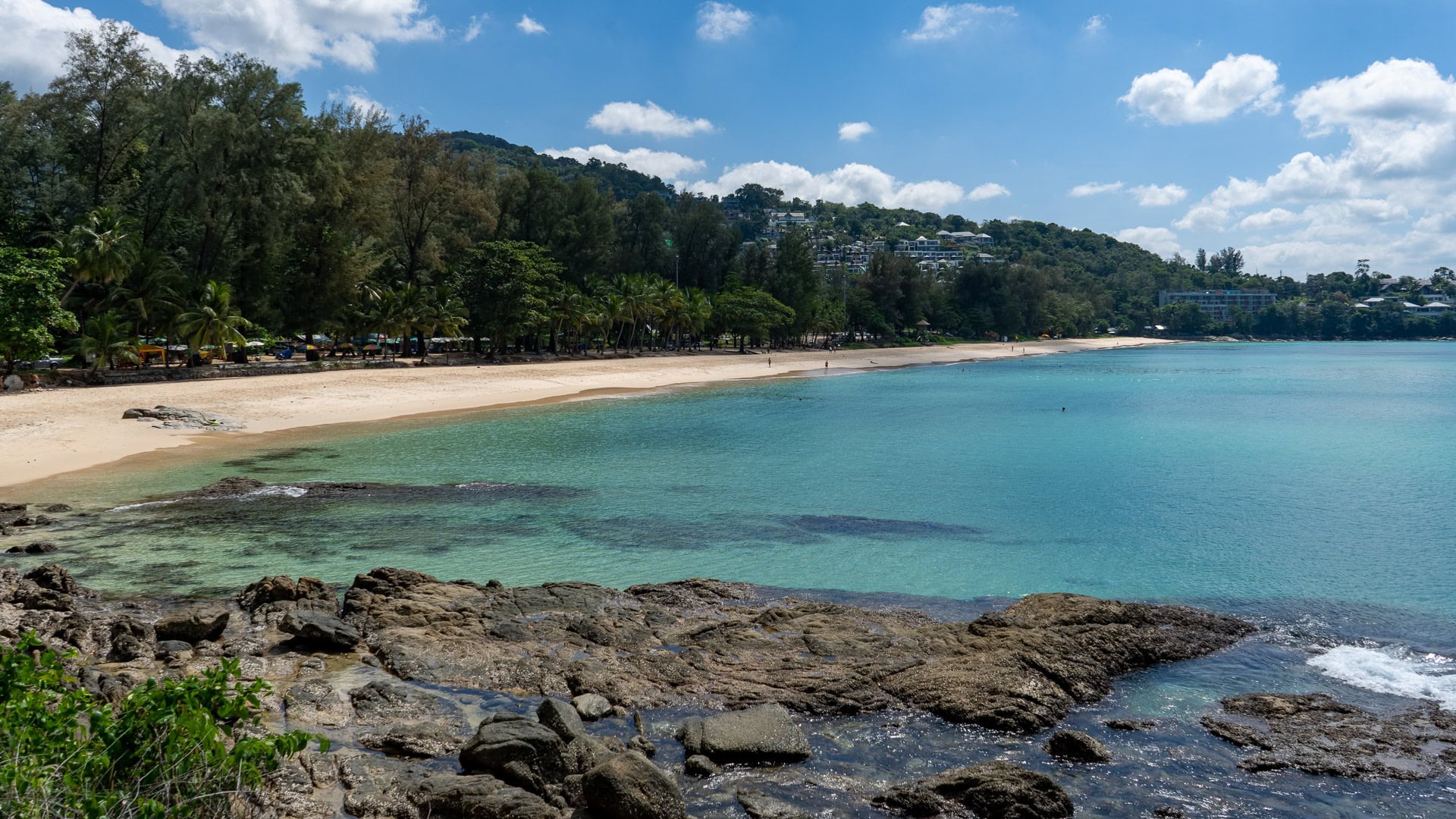 Mid-beach view toward northern headland with resort buildings visible.