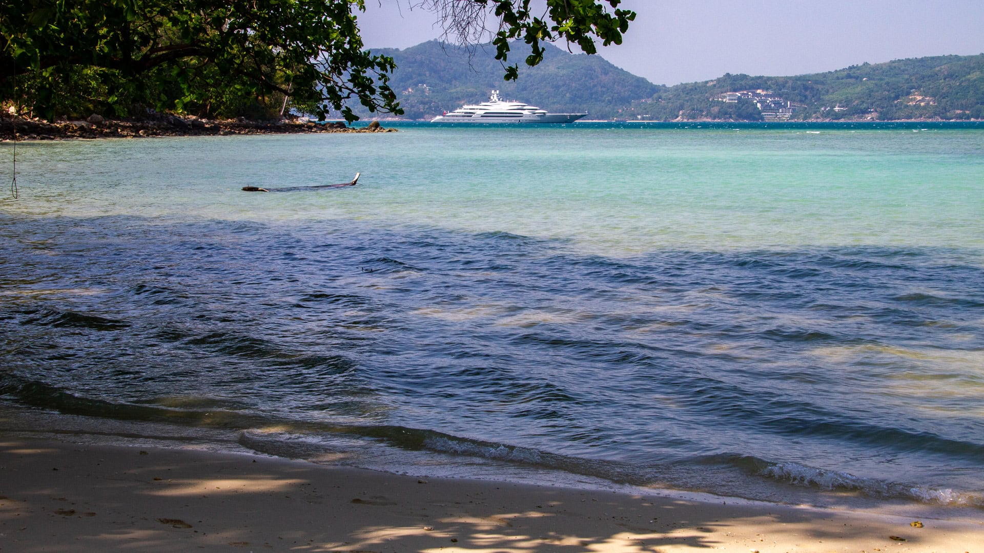 Tri Trang Beach Phuket sandy shoreline with tree shade and distant hills