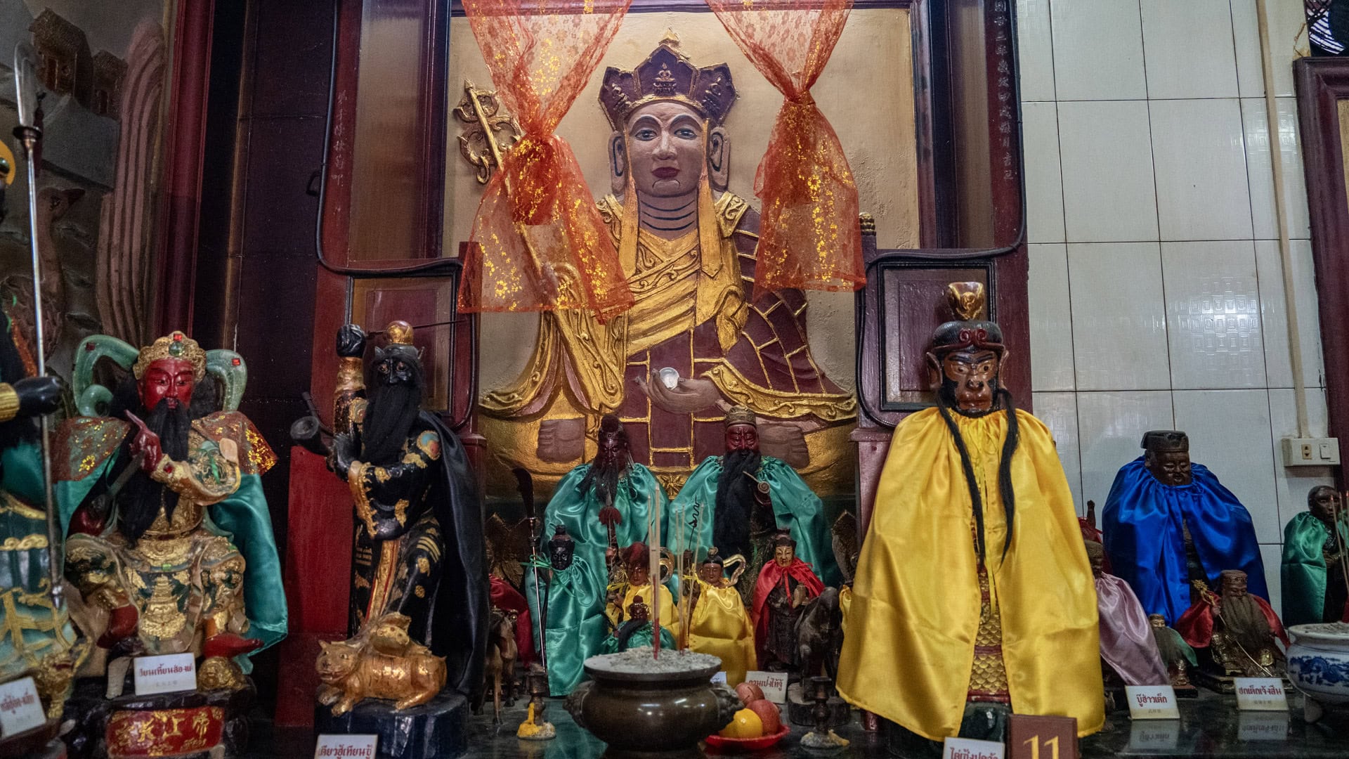 A large relief figure in gold and brown fills the back wall above small shrine statues in coloured robes, with an incense pot and offerings in front.