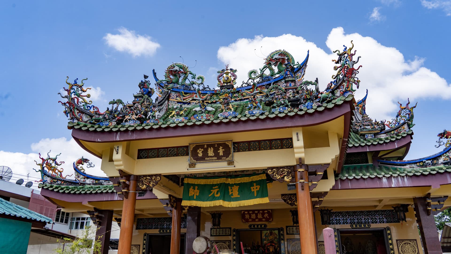 The shrine entrance is seen from below, with carved roof ridges, green tiles, Chinese signboards, and multicoloured dragon figures above the portico.