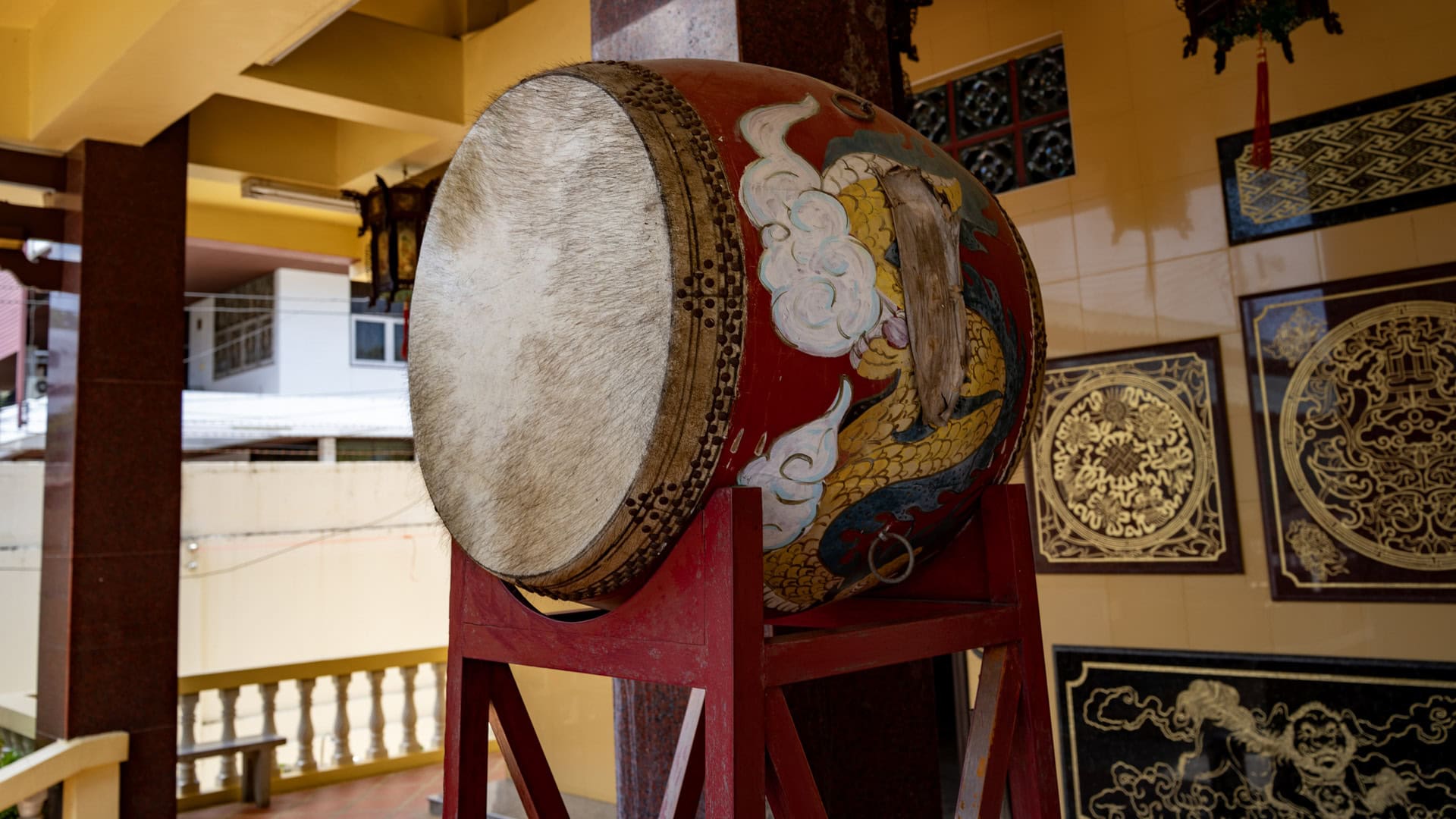 A painted ceremonial drum stands on a red timber frame beside the entrance, its dragon-decorated body set against black-and-gold wall panels.