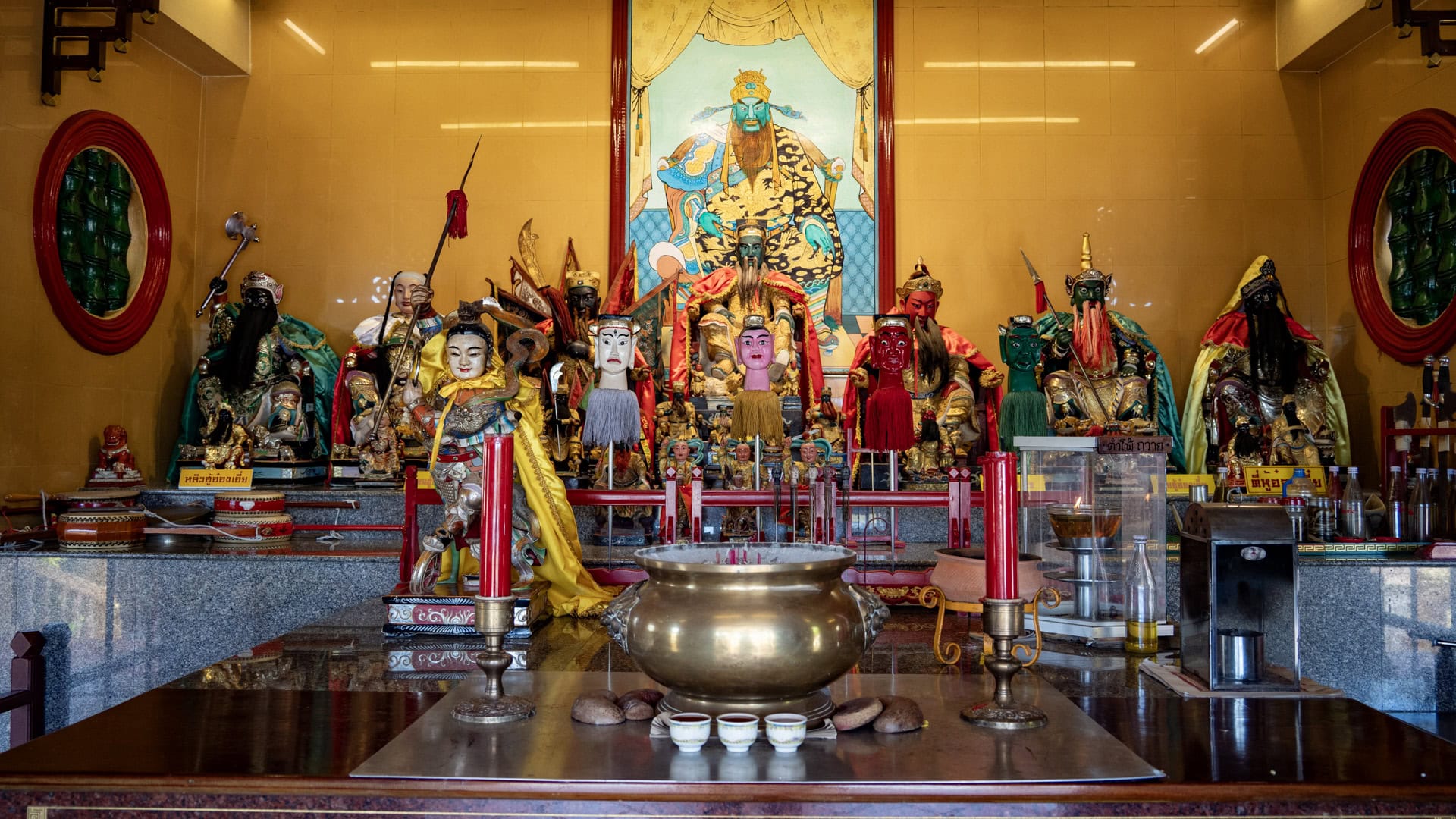 A brass incense burner and red candles stand before a crowded altar of deity figures inside the shrine’s main hall.