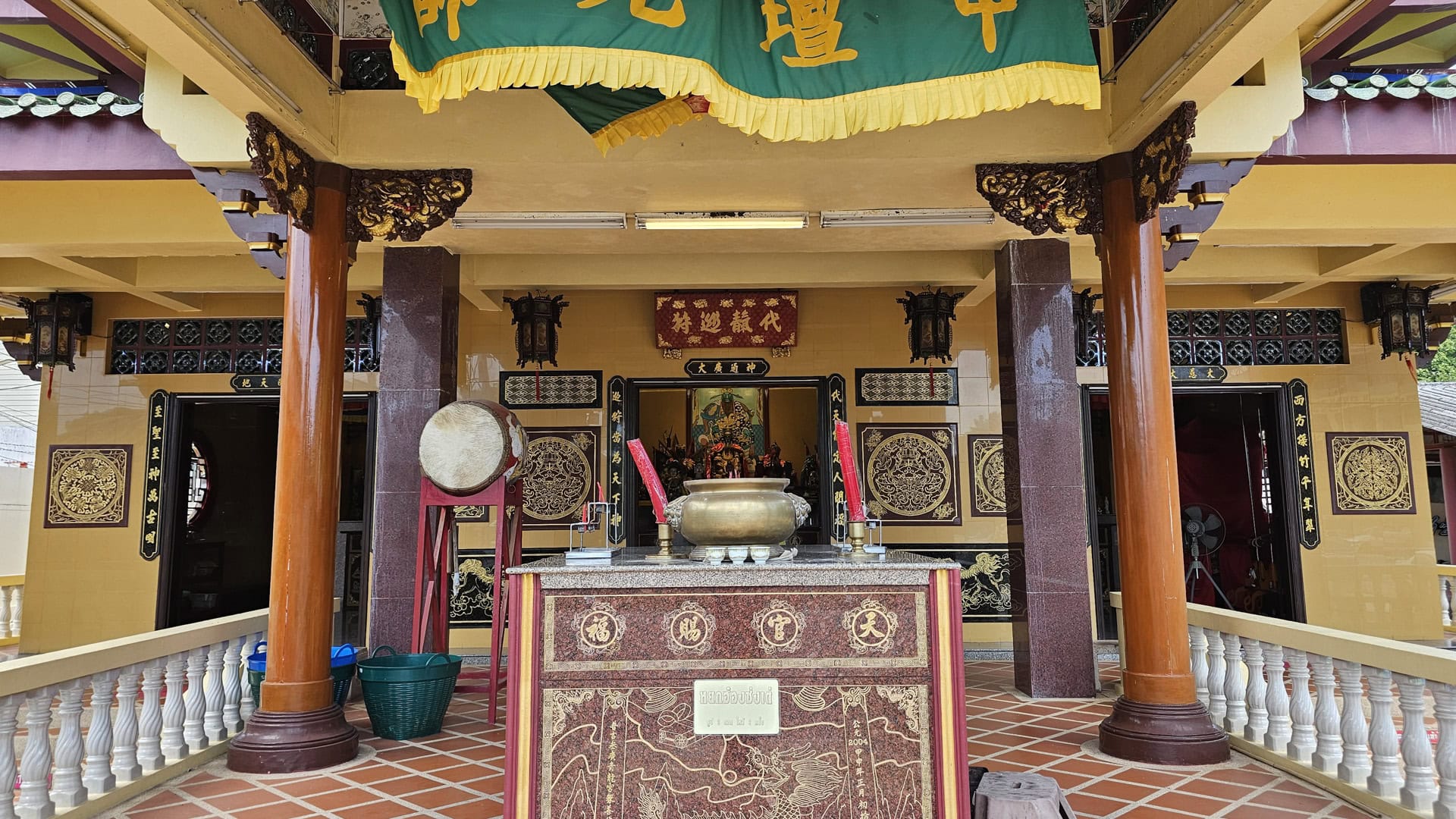The shrine entrance is framed by wooden columns, with a central incense burner, two red candles, and a drum visible beside the doorway into the hall.
