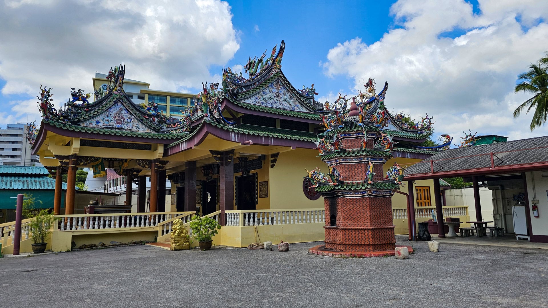 A side view of the shrine shows decorated green roofs, a brick furnace-like structure with dragon ornament, and an open paved yard.